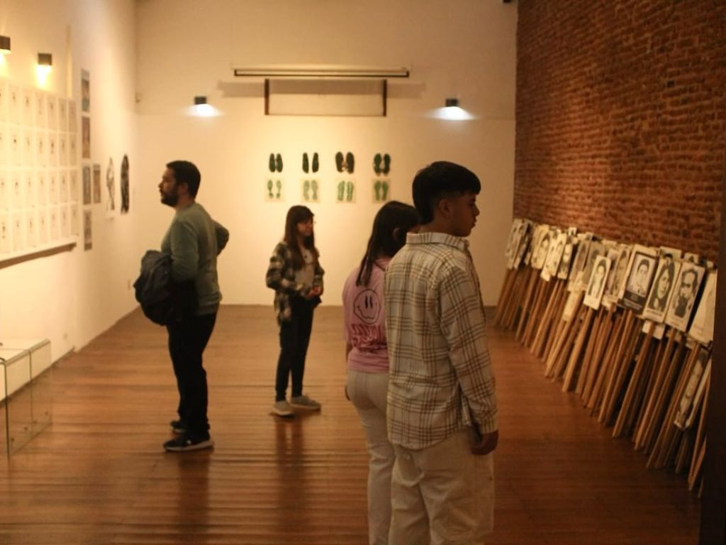 Fotografía interior tomada en el Museo de la Memoria. En ella se puede ver una sala de la muestra Giro Gráfico con varias personas observando la muestra