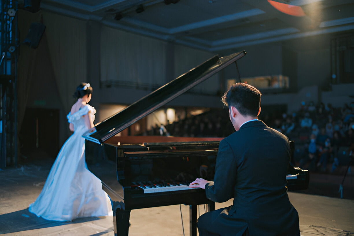 Imagen de mujer cantando con vestido blanco y hombre sentado al piano