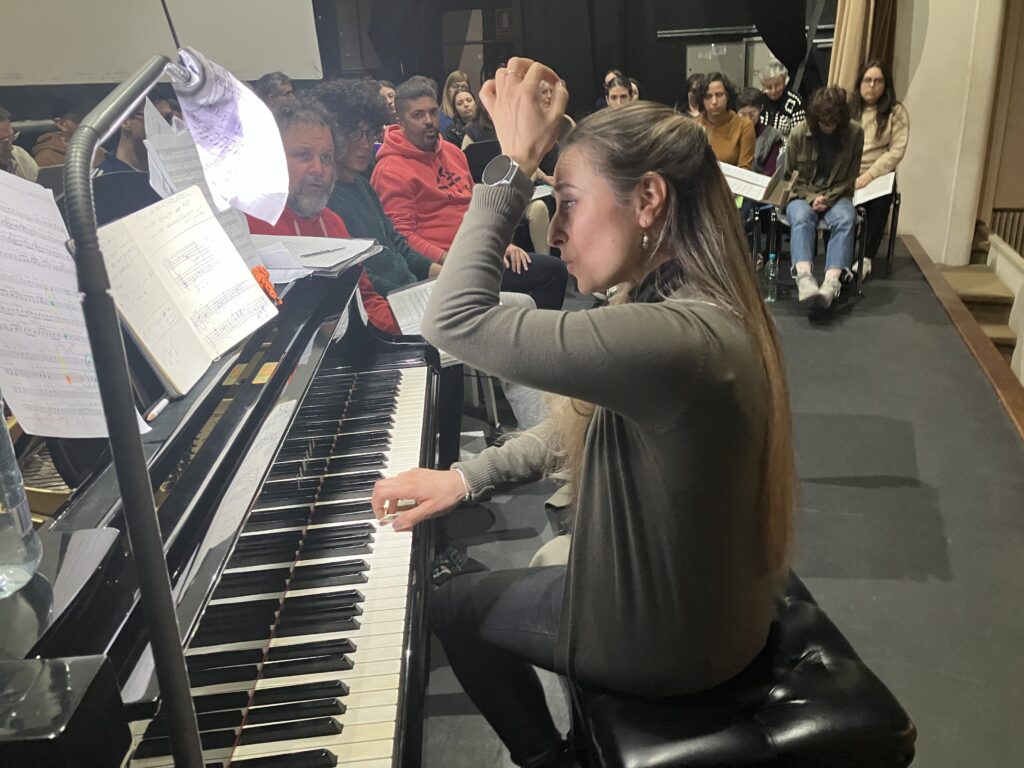 Chiara Daniele frente a los integrantes del coro dando indicaciones para la interpretación en el piano