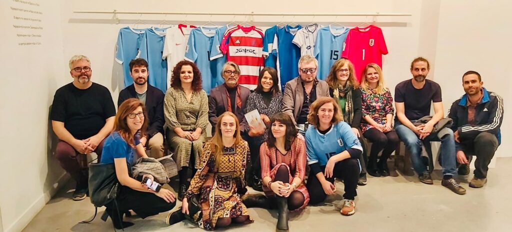 Imagen del vestuario de un equipo de fútbol donde se ven de fondo camisetas de selecciones nacionales de fútbol colgadas y delante de ellas varias personas sentadas posando a cámara, algunas de ellas con camisetas puestas