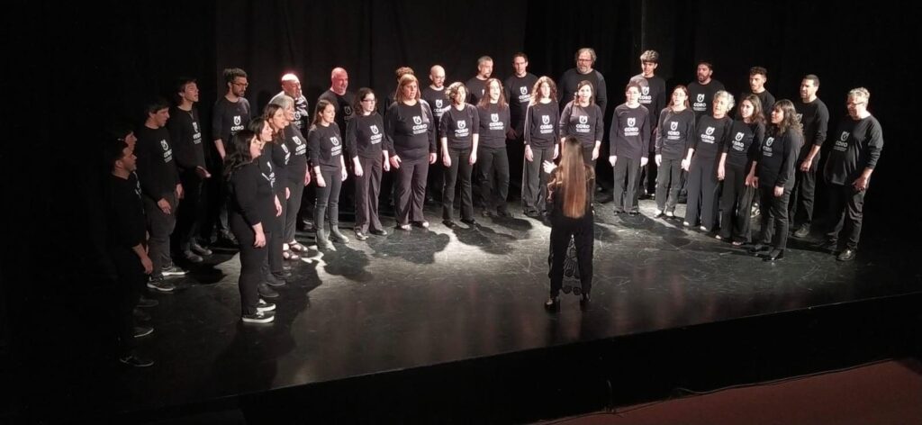 Fotografía donde se ve en fondo negro en el escenario las personas que integran el coro de la Udelar